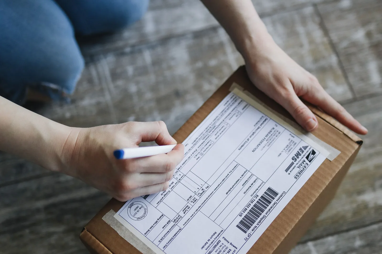 Cardboard parcel-এর shipping label-এ pen দিয়ে address লিখছেন একজন ব্যক্তি