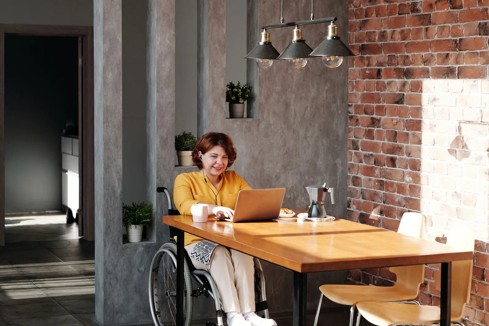 Wheelchair ব্যবহারকারী একজন নারী accessible home workspace-এ laptop ব্যবহার করছেন