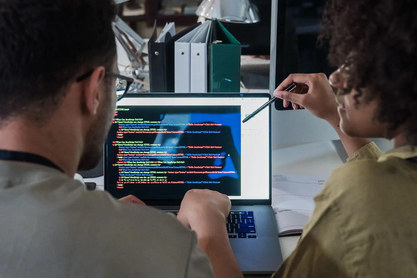 Office-এ দুই developer laptop screen দেখে নতুন software workflow আলোচনা করছেন
