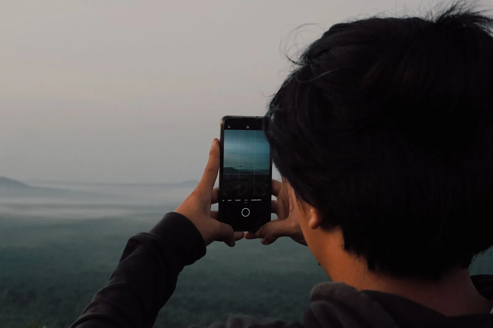 একজন ব্যক্তি smartphone দিয়ে পাহাড়ি landscape-এর ছবি তুলছেন